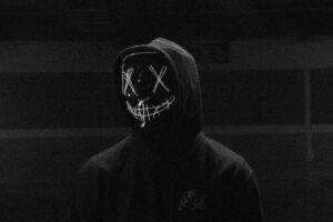 Eerie image of a person in a glowing LED mask and hoodie in a dark setting.