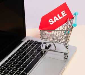 Mini shopping cart with sale tag on laptop for online shopping theme.